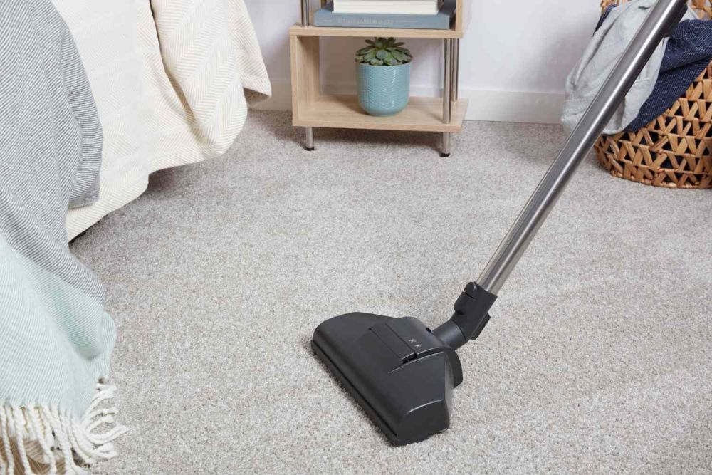 A vacuum cleaner placed on the floor before a bed, showcasing a carpet cleaning service in Aurora, CO.