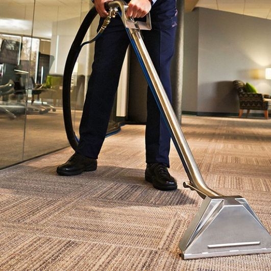 A man cleans a carpet with a vacuum cleaner, representing a carpet and rug cleaning service in Aurora, CO.