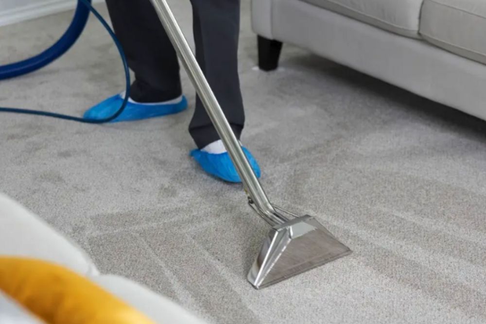 Individual using a vacuum cleaner on a carpet during a carpet restoration service in Aurora, CO.