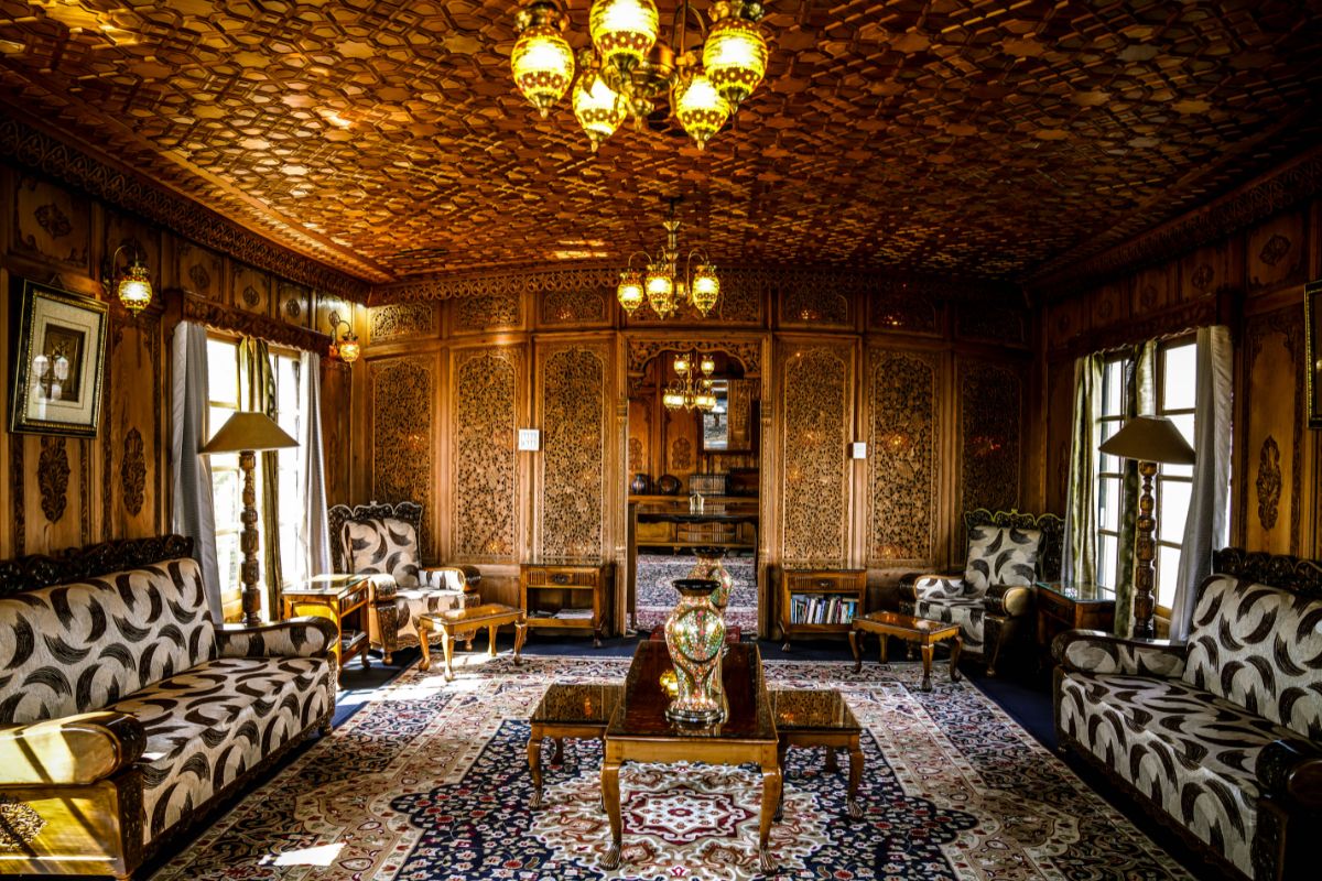 A richly decorated living room featuring intricately carved wooden walls, ornate lamps, plush seating, and a vibrant rug.
